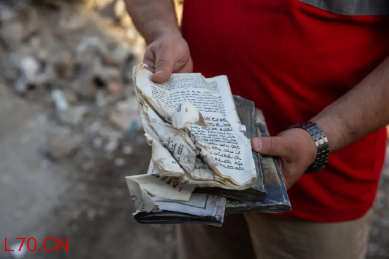 一人手持受损的书页，背景是瓦砾。从废墟中找回的受损《托拉》经卷。